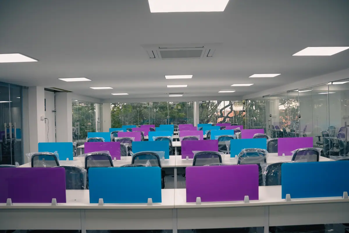 Open workspace with blue and purple desk partitions facing a wall of glass and trees